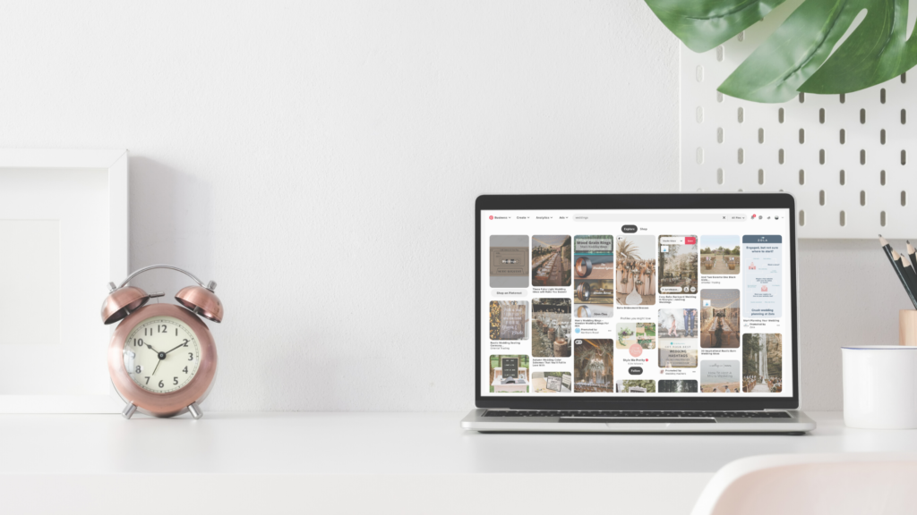 laptop with a pinterest page on a white desk next to a rose gold clock