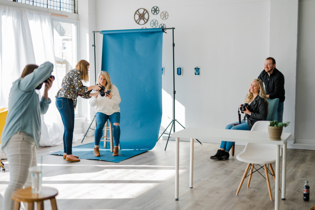 a group of photographers taking photos of each other in a bright white studio in front of a blue backdrop
