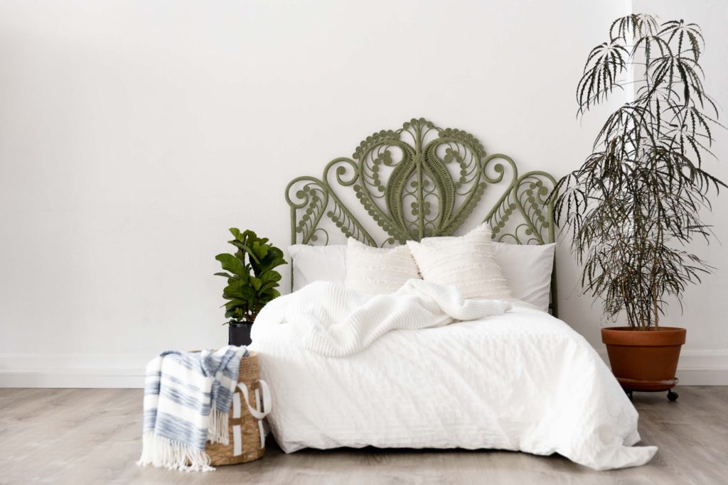 a photography set featuring sage green wicker headboard with a white bed and plants