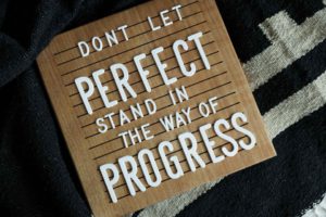 white letters on a brown letterboard spelling out progress over perfection.