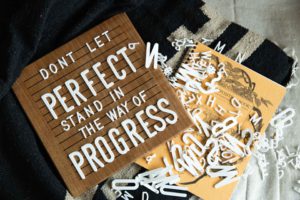 white letters on a brown letterboard spelling out progress over perfection.